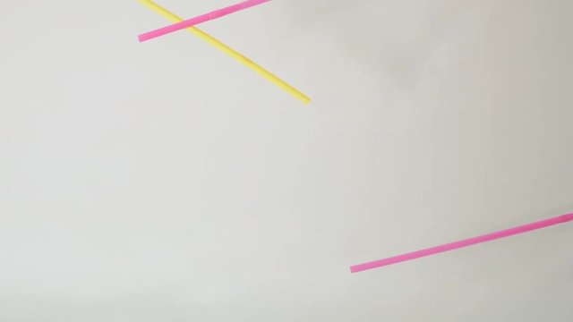 Brightly colored Bent plastic single use straws dropping into water against a neutral white background