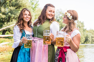 Oktoberfest Freunde in Lederhosen und Dirndl trinken Bier an der Isar