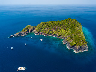 Aerial drone view of tourist boats around a beautiful, jungle covered tropical island surrounded by shallow coral reef