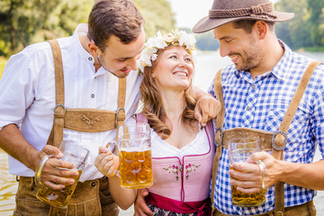 Oktoberfest Freunde in Lederhosen und Dirndl trinken Bier an der Isar