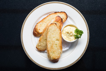 Close up top view garlic  bread baked sliced with mayonnaise and parsley on white plate