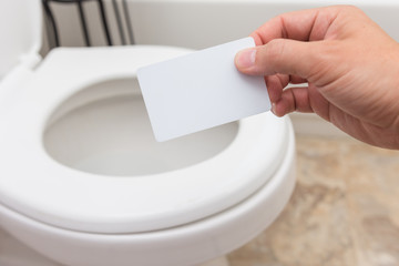 Holding blank card (credit card, membership card, coupon, drivers license) into toilet; bright and clean; finance concept