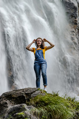 Naklejka premium Young teenage girl standing on the big stone near waterfall
