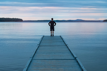 A man on a dock looking at a lake. - Powered by Adobe