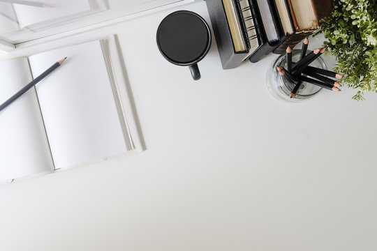 Flat lay, top view office table desk. Workspace with notebook, book, office supplies, pencil, green leaf, and coffee cup on white desk.