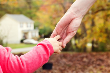 Toddler girl holding hands with her father outside on a fall day