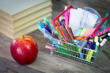 Back to School. Accessories in the basket, books and fresh apple on wooden background