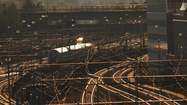 AERIAL SHOT of a train moving slowly on its tracks with people and traffic on a bridge in a lovely sunset in Stockholm, Sweden. Filmed in SLOW MOTION.