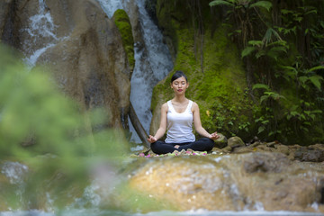 beautiful woman meditating on stone at waterfall in the forest.