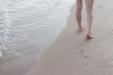 Beach travel alone - woman walking alone on sand beach leaving footprints in the sand Closeup detail of female feet and golden sand