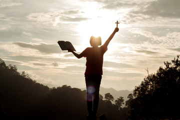 silhouette human praying to the GOD while holding a crucifix symbol with bright sunbeam on the sky
