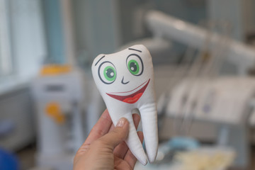 Smiling tooth in female hand on dentist office background.Tooth smiling.White healthy teeth...