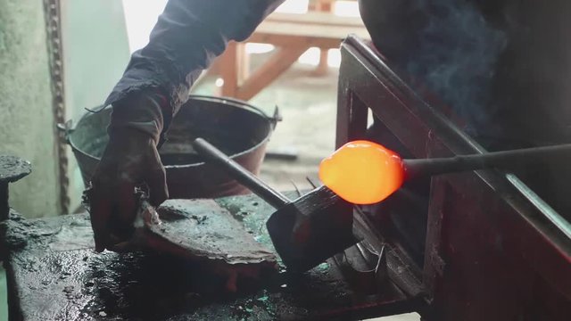 A man molding hot glass while seated