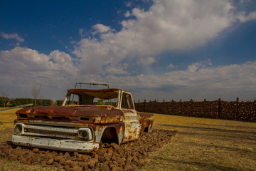 Wreck of an old rusted pick up truck in a deserted playground standing on a bed of stones image in landscape format with copy space