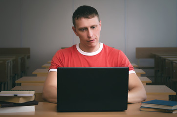 Curious student boy sitting by the school desk and working with laptop.
