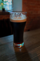 Glass of dark beer. Selective focus. Craft beer stands on dark vintage wooden table in the pub. Brasserie in loft style design.