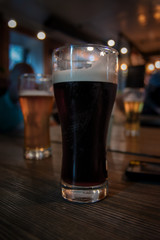 Glass of dark beer. Craft beer with foam stands on dark vintage wooden table in the bar. Brasserie in loft style. 