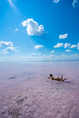 A beautiful woman in a bikini is lying on her stomach in a pink salt lake. The red-haired woman lies, sexually bending in her back and lifting her ass.