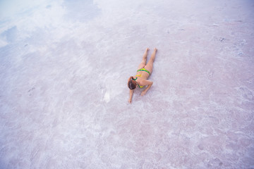 A beautiful red-haired woman in a bikini lies on her stomach in a pink salt lake. the bottom of the lake is covered with crystallized salt