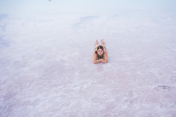 A beautiful red-haired woman in a bikini lies on her stomach in a pink salt lake. the bottom of the...