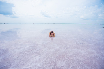 A beautiful red-haired woman in a bikini lies on her stomach in a pink salt lake. the bottom of the...