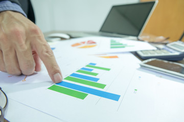Business documents on office table with laptop, smart phone  and graph financial and man working in the background. Business concept.