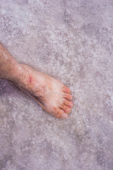 Bare feet of men in the pink salt lake Bursol, Altai territory. Salt Deposit. Unique pink lake.