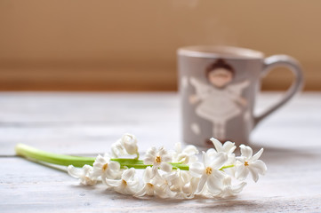 Fototapeta na wymiar Cup of coffee and white flower on a light wooden background