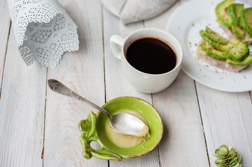 Cup of coffee and slices of avocado on a white plate on a light wooden background