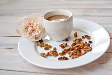 Cup of coffee with milk, nuts, sweets and a bud of a peony on a white saucer