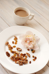 Cup of coffee with milk, nuts, sweets and a bud of a peony on a white saucer