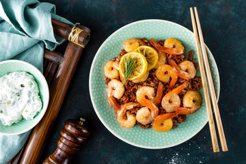 Prawns roasted on grill and boiled brown rice on plate. Grilled shrimps, prawns with rice. Seafood. Asian cuisine. Top view. Dark background