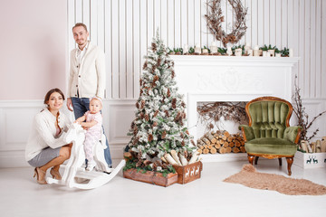 Loving family Merry Christmas and Happy New Year. Cheerful pretty people. Mom, dad and little daughter . Parents and baby child having fun near Christmas tree and white fireplace indoors.