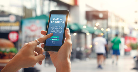 Man hands using smartphone for online shopping on city street background.  E-commerce icon network on screen. Digital marketing and Mobile payments. Online shopping concepts