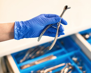 Doctor's hand wearing a disposable medical gloves holding a stainless steel nasal speculum for ENT...