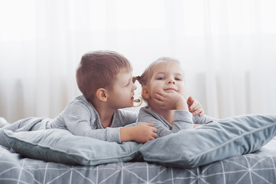 Kids Playing In Parents Bed. Children Wake Up In Sunny White Bedroom. Boy And Girl Play In Matching Pajamas. Sleepwear And Bedding For Child And Baby. Nursery Interior For Toddler Kid. Family Morning