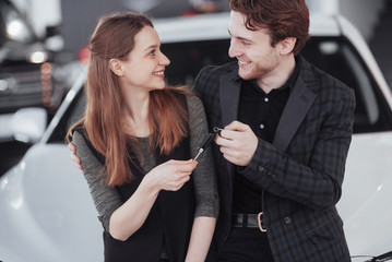 Proud owners. Beautiful young happy couple hugging standing near their newly bought car smiling joyfully showing car keys to the camera copyspace family love relationship lifestyle buying consumerism