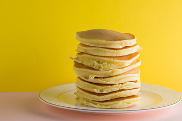 Pancakes on a yellow pink background. Many pancakes on a white plate with copy space. Delicious dish for breakfast in the style of pop art. Festive food on a colorful background