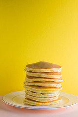 Pancakes on a yellow pink background. Many pancakes on a white plate with copy space. Delicious dish for breakfast in the style of pop art. Festive food on a colorful background