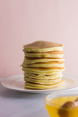 Pancakes on a white pink background. Hot pancakes with honey on a white plate with copy space. Delicious dish for breakfast in the style of pop art. Honey flows down from a wooden stick on a dish