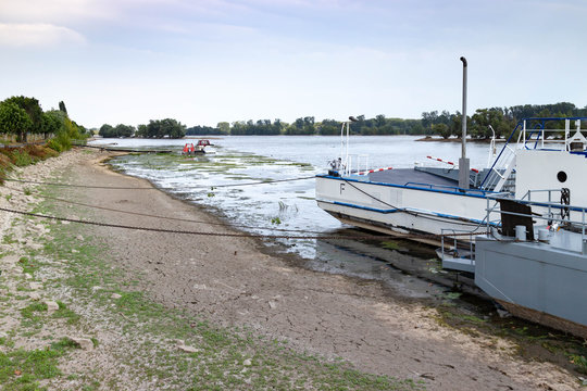 Am Ufer liegende Fähre, im Vordergrund der vertrocknete, aufgeplatzte Boden, im Hintergrund einzelne Boote umgeben von Algen und Schlingpflanzen