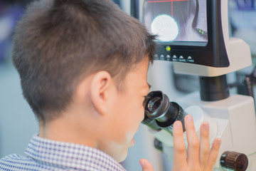 Little boy leaning to use microscope in the science lap at school