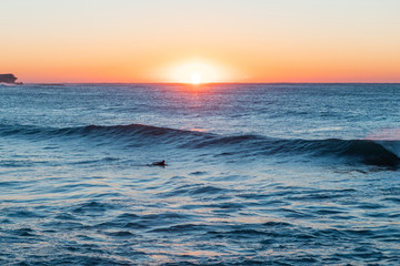 Silhouette of surfer swimming on the beach at sunrise time.