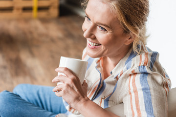 high angle view of smiling mature woman holding cup and looking away
