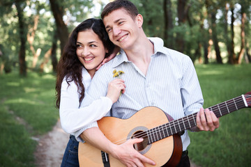 Naklejka premium young couple walking in the forest and playing guitar, summer nature, bright sunlight, shadows and green leaves, romantic feelings