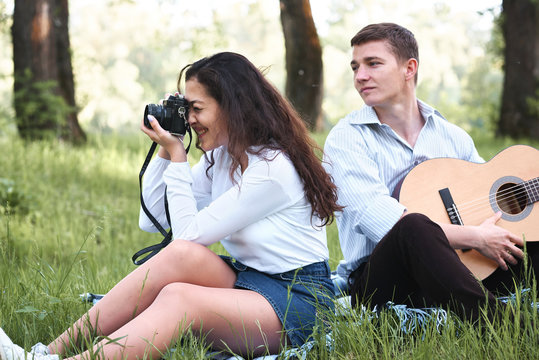 young couple walking in the forest and playing guitar, taking photo on old camera, summer nature, bright sunlight, shadows and green leaves, romantic feelings