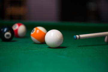 Sport billiard balls on green billiard table in pub. Player is about to hit the ball, focusing on his shot. On going billiard game. Competitive players trying to find out the winner of the round.