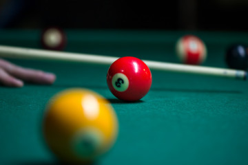 Sport billiard balls on green billiard table in pub. Player is about to hit the ball, focusing on his shot. On going billiard game. Competitive players trying to find out the winner of the round.