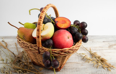 basket with fruit plum, grapes, apple, pear. put on a wooden board