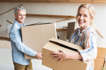 happy senior couple holding cardboard boxes and smiling at camera during relocation